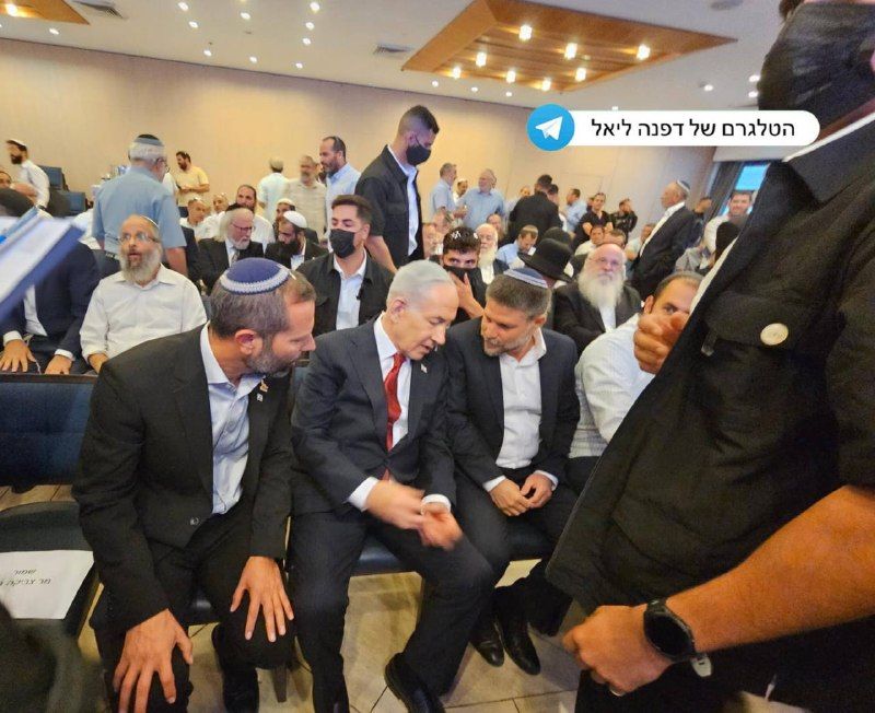 בנימין נתניהו ובצלאל סמוטריץ׳ יושבים לצד משתתפים באולם מלא אנשים.