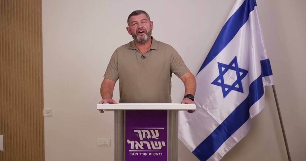 דורון וינטר עומד מאחורי דוכן לצד דגל ישראל.