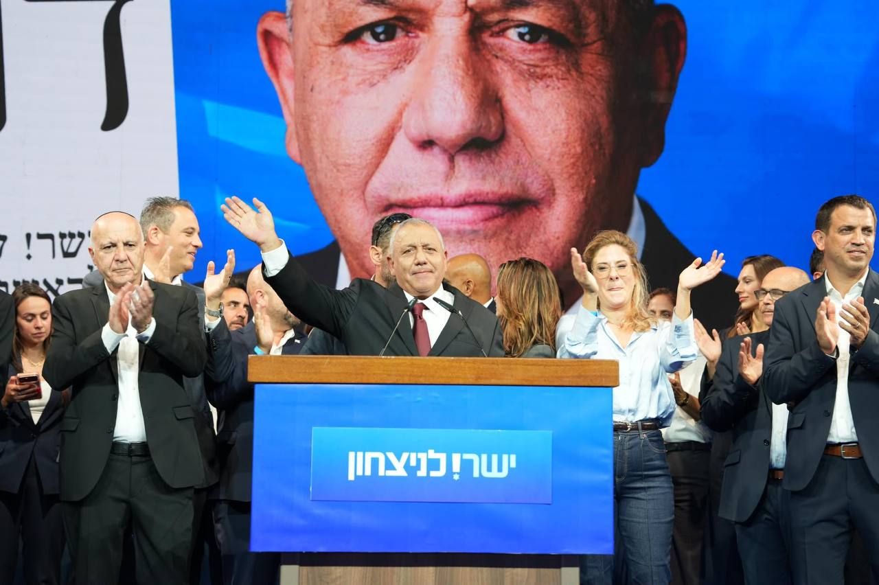 גדי איזנקוט מניף יד מאחורי דוכן, וסביבו אנשים מוחאים כפיים.