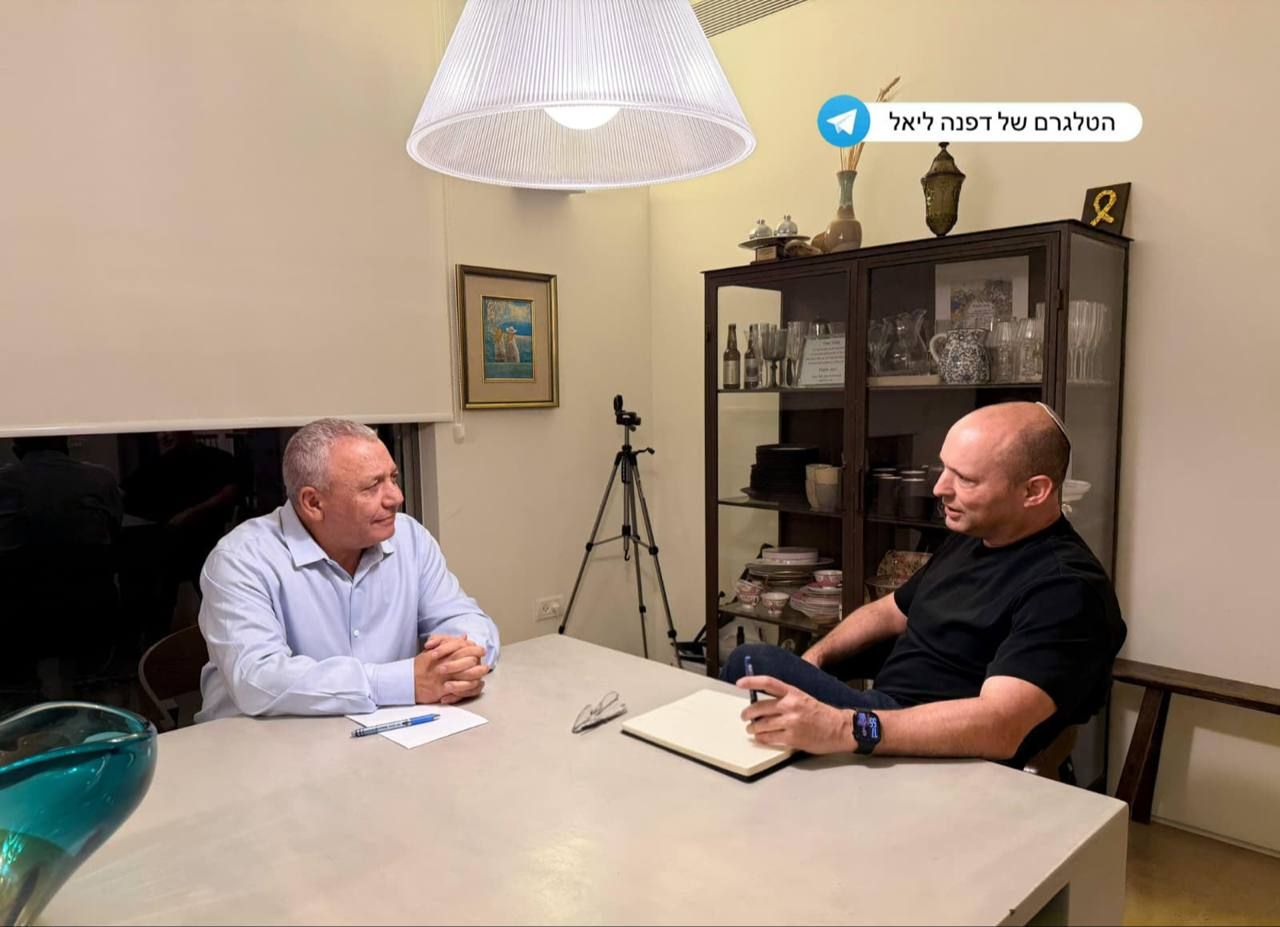 נפתלי בנט וגדי איזנקוט יושבים משני צדי שולחן בחדר.